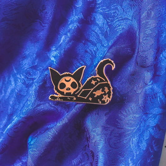 Cat-shaped pin with skull design on a blue textured fabric background